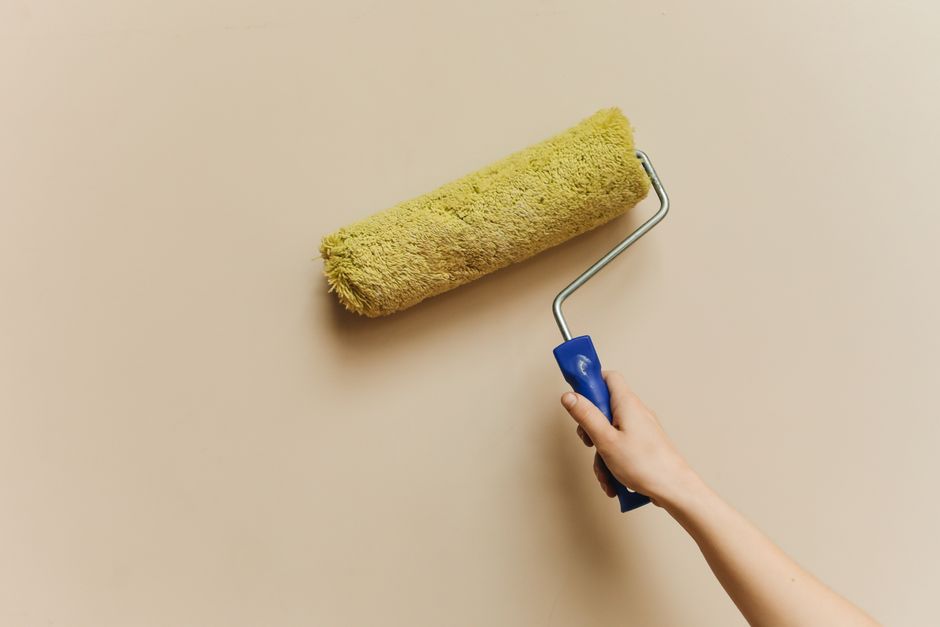 Hand rolling beige paint onto an interior wall
